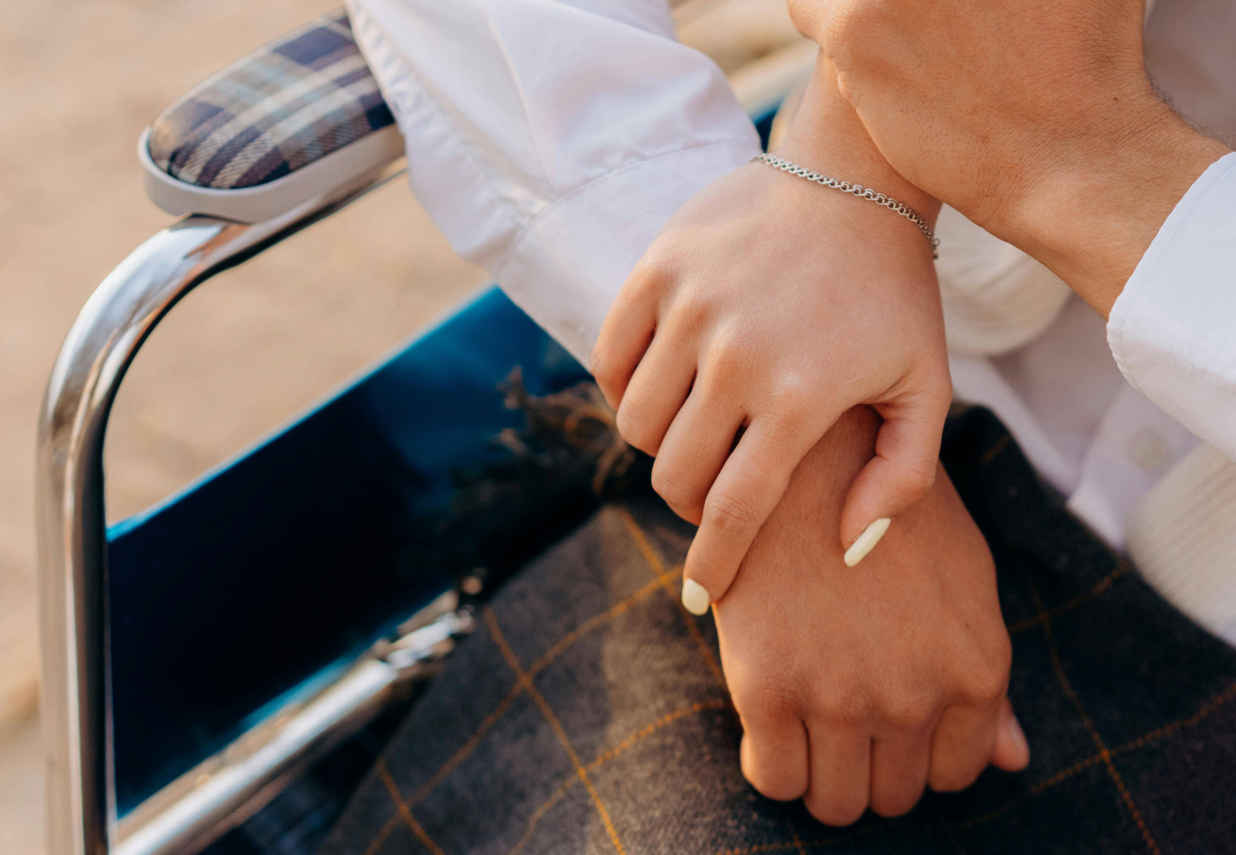 Closeup of a couple holding hands, one of them is a wheelchair user